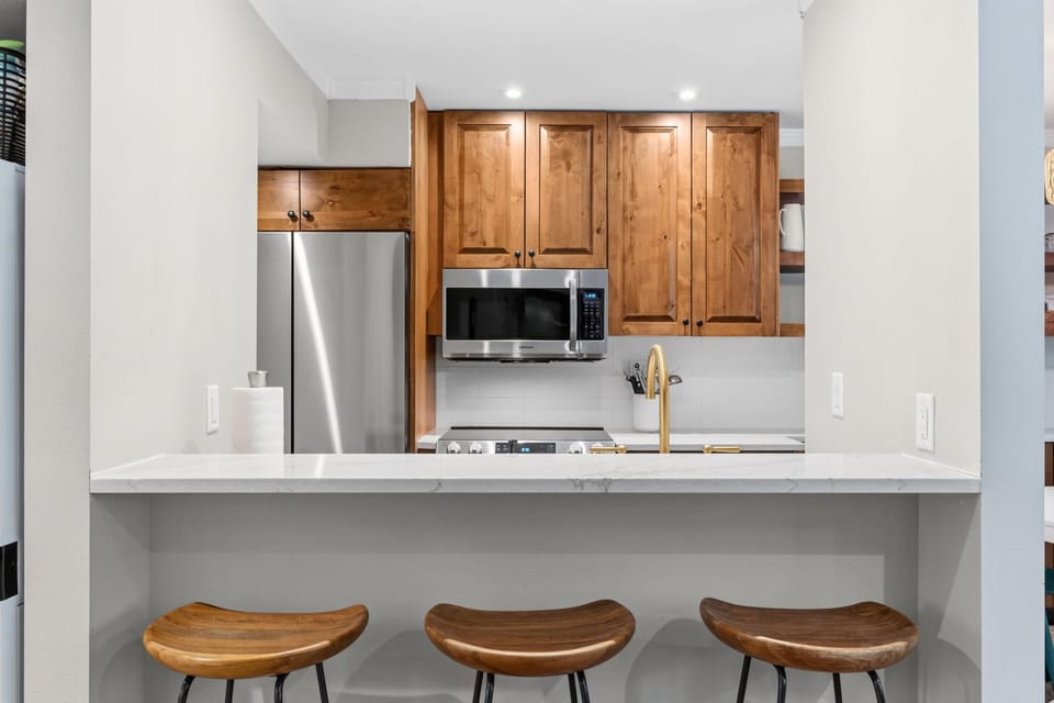 Your fully equipped kitchen features warm wood cabinetry, stainless steel appliances, and a sleek breakfast bar with modern seating—perfect for morning coffee or meal prep during your stay.