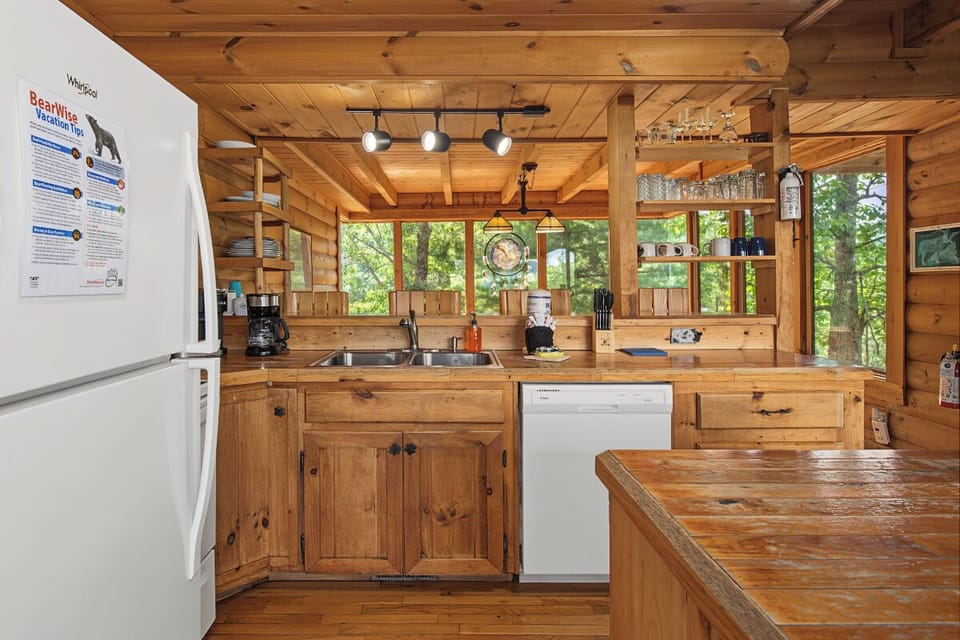 Step into your cozy cabin kitchen, where rustic wood beams frame forest views through every window. Prepare meals with full appliances while sunlight streams in and nature surrounds you—your perfect mountain escape awaits.