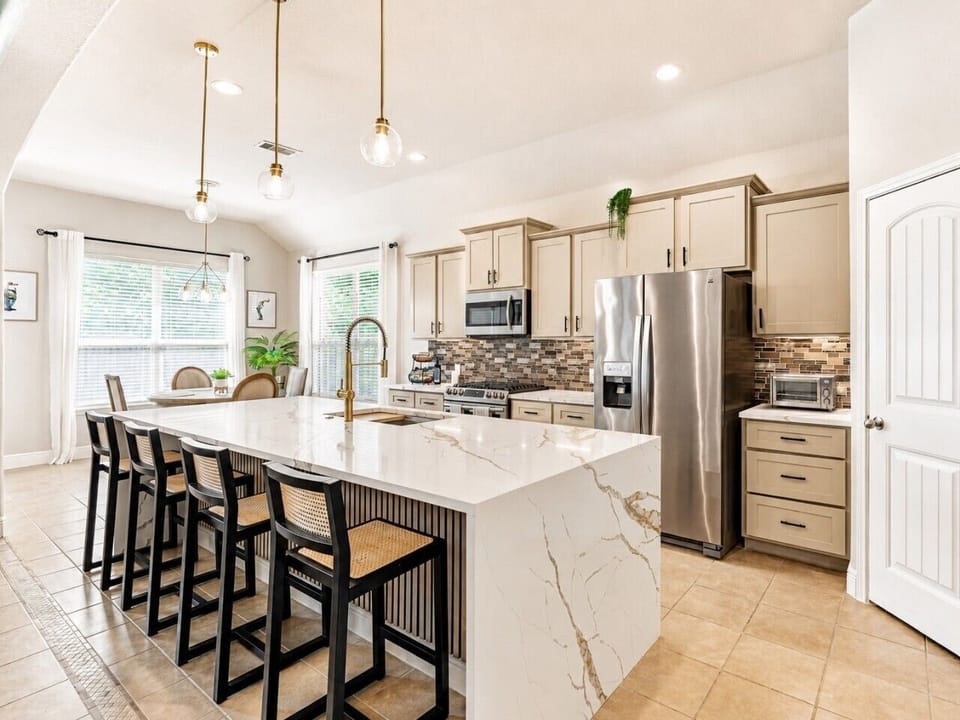 Bright kitchen with island seating, stainless appliances, and pendant lights.
