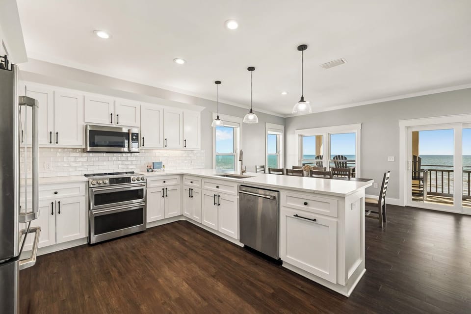Your dream coastal kitchen awaits with pristine white cabinetry, gleaming countertops, and stunning ocean views through every window—perfect for preparing meals while soaking in the seaside atmosphere.