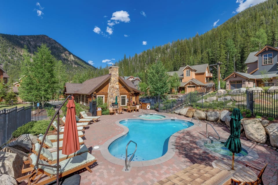 A mountain-framed outdoor pool and hot tub area surrounded by pine forests, offering peaceful alpine scenery and relaxation at this vacation retreat.