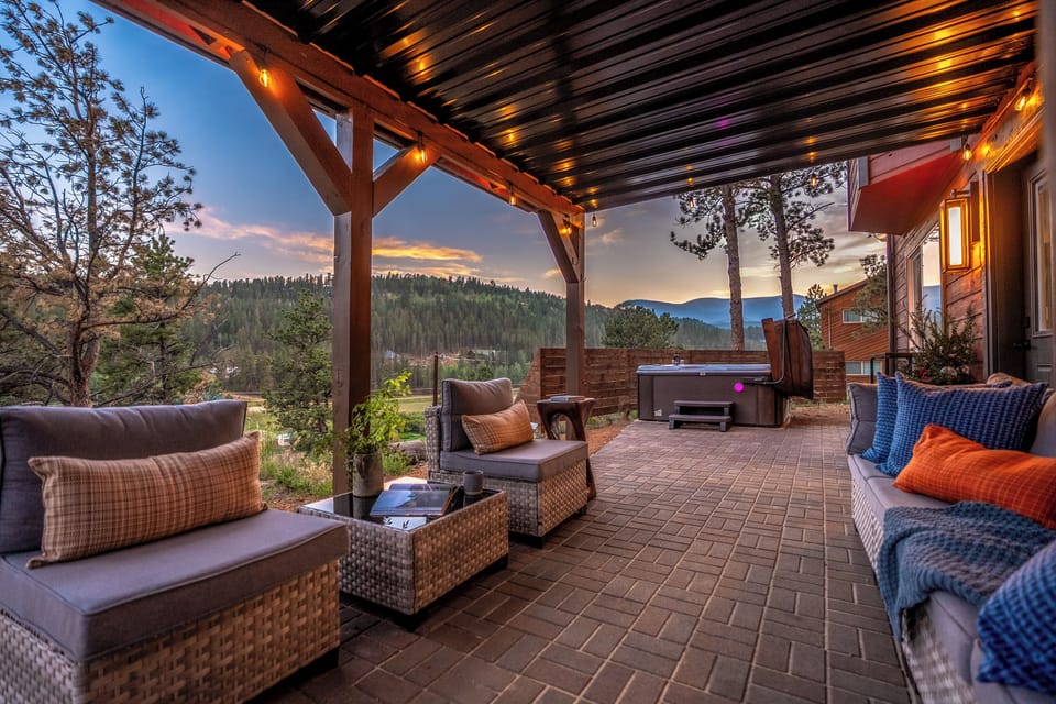 Covered patio with hot tub, cozy seating, and scenic mountain sunset views
