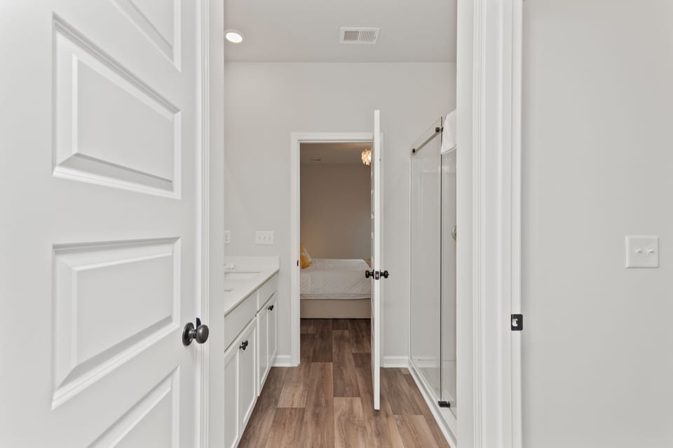 Bathroom with a glass shower and vanity leading into the bedroom.
