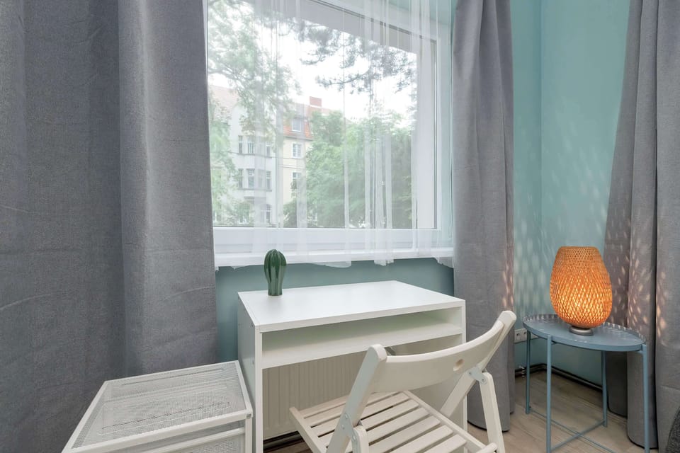A practical bedroom combines a comfortable sleeping area with a dedicated workspace, featuring a desk positioned near the window for natural light. Functional furnishings and a bright interior make the room suitable for both relaxation and productivi