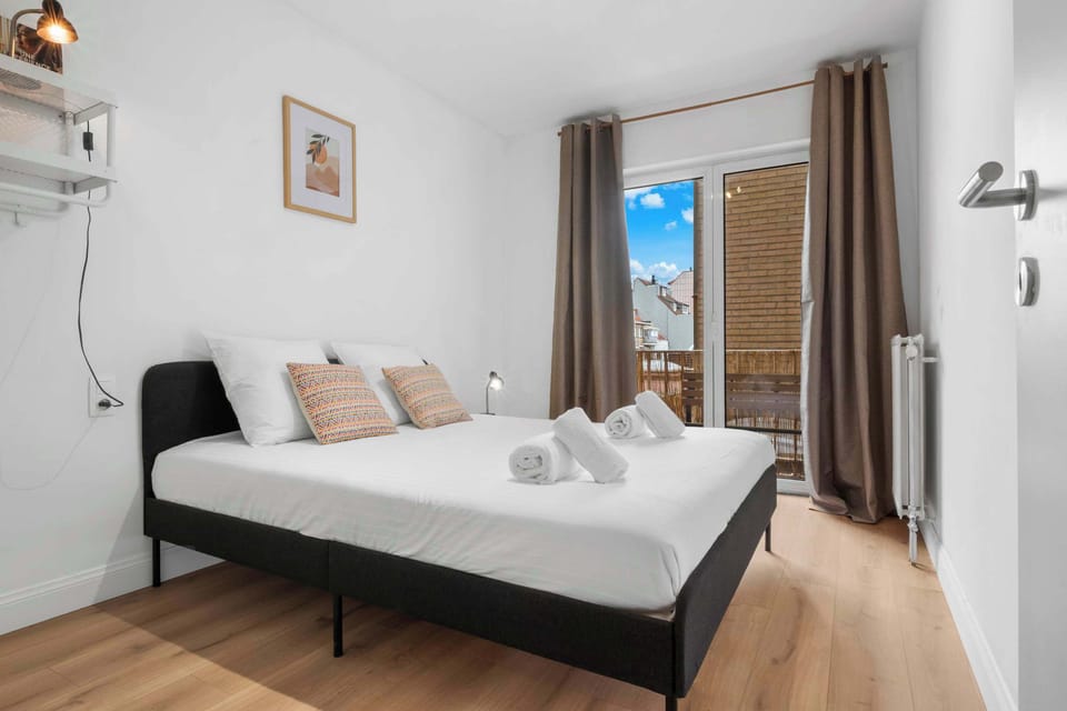Bright bedroom with a comfortable double bed, fresh towels and a balcony door letting in natural light, in this stylish 1-bedroom apartment in central Knokke.