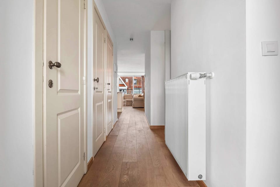 Bright hallway with white doors and warm wood flooring connecting the rooms of this Knokke duplex.