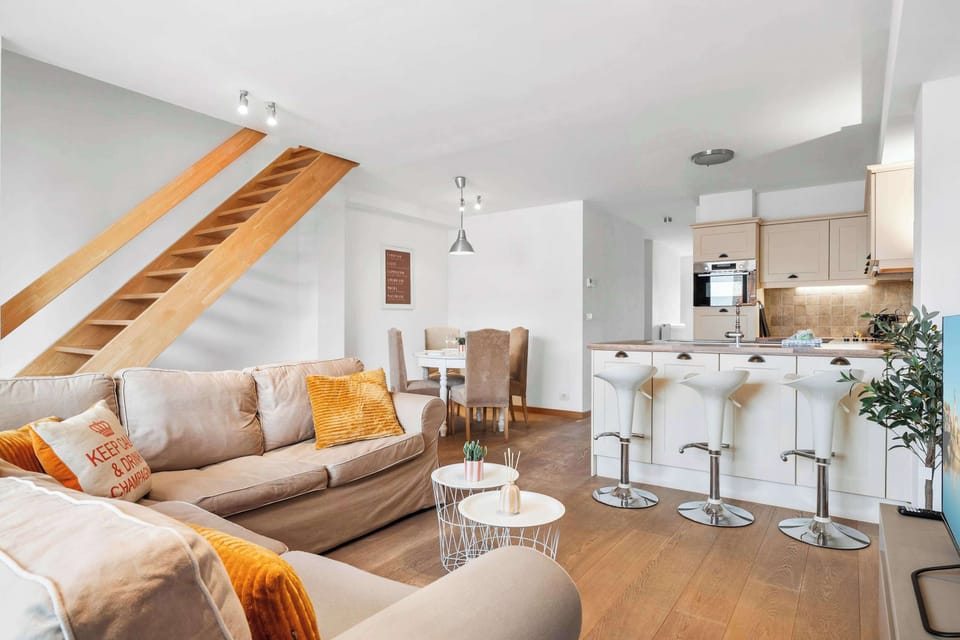 Relaxed lounge with sofa and bright cushions, opening to the kitchen – sociable duplex living in Knokke.