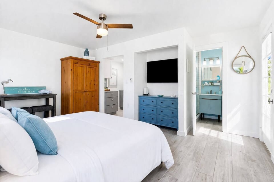 Stylish, airy bedroom featuring plush bedding, coastal accents, and open layout connecting to bath—perfect for a restful getaway.