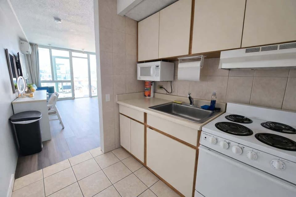 Bright and functional kitchen with full-size stove, microwave, and ample cabinet space — everything you need to cook and dine comfortably. The open layout flows seamlessly into the living area, filled with natural light from floor-to-ceiling windows.