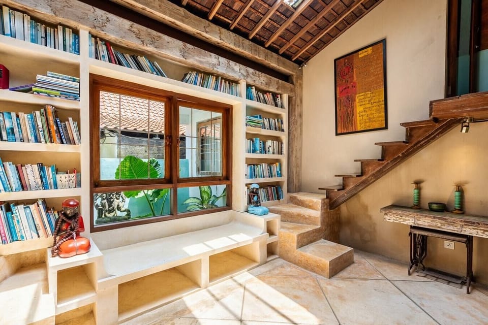 Another angle of the inviting reading nook, showcasing the same comfortable bench and extensive bookshelf. The large windows frame a stunning view of the tropical garden, creating a serene and inspiring environment.