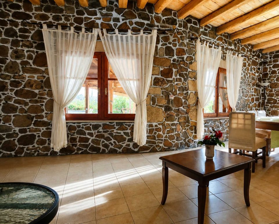 Settle into a living and dining area with grounded stonework, timber overhead, and plenty of room to gather.
