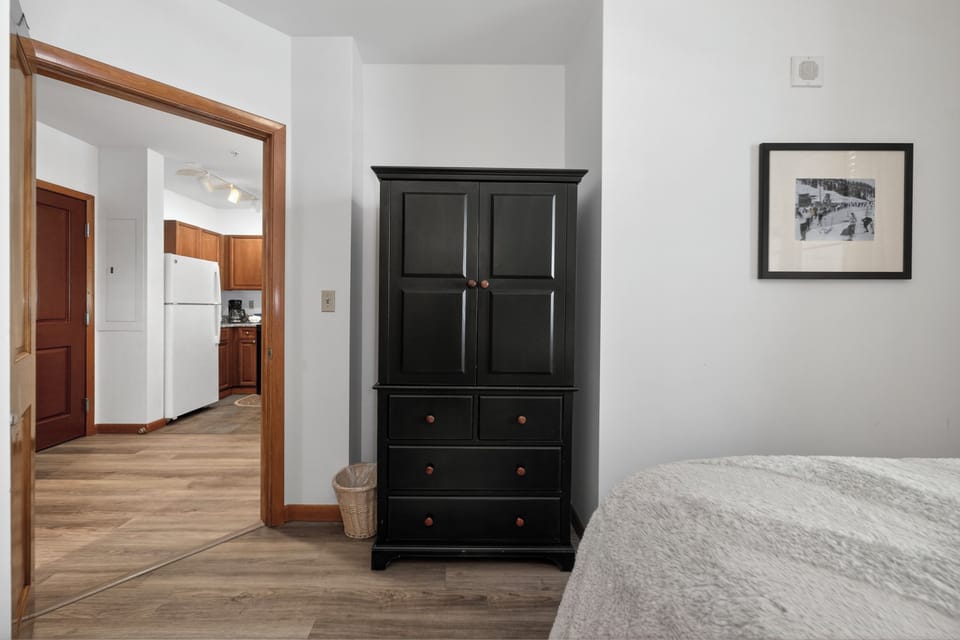 Your bedroom opens to a fully equipped kitchen, offering easy morning coffee runs. The elegant wardrobe provides ample storage, while charming vintage artwork adds character to your restful retreat.