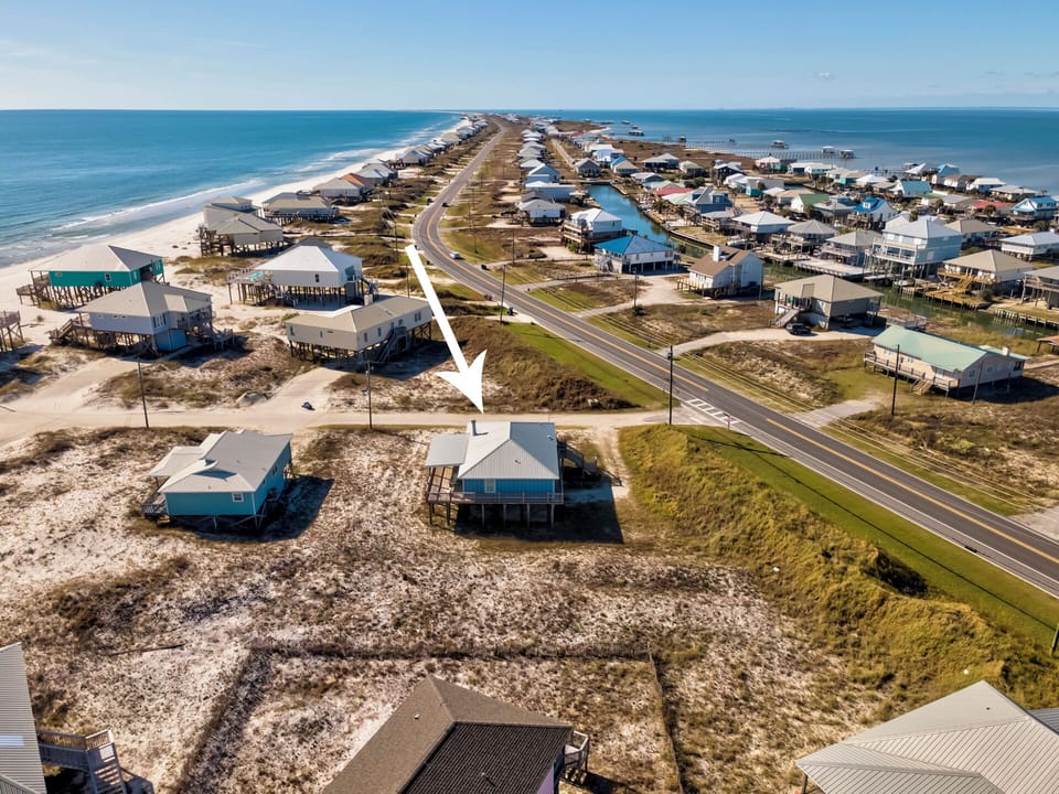 Aerial view of Sea Glass located in charming Dauphin Island beachfront community with vacation homes lining both sides of the coastal highway, offering direct access to sandy shores.