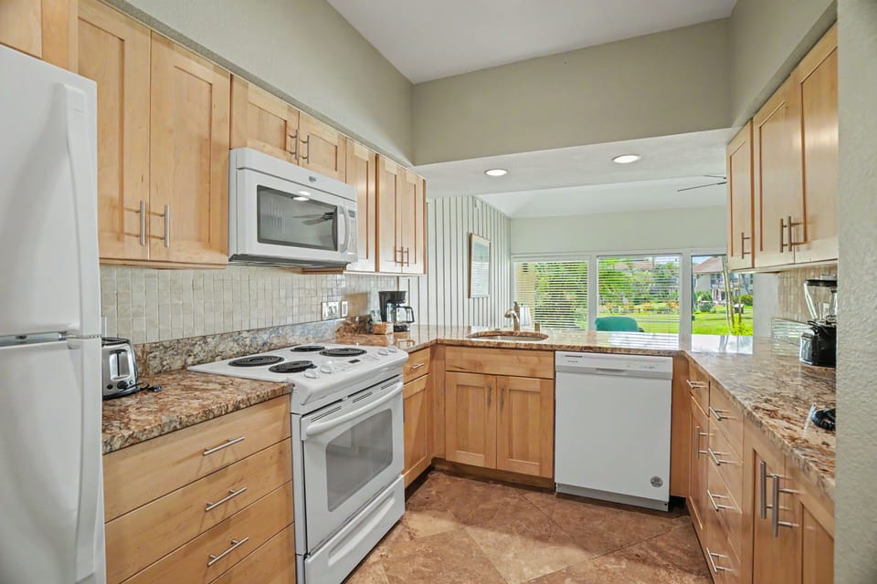 Your fully equipped kitchen features granite countertops, modern appliances, and natural light streaming through windows overlooking the pool area—perfect for preparing meals during your stay.
