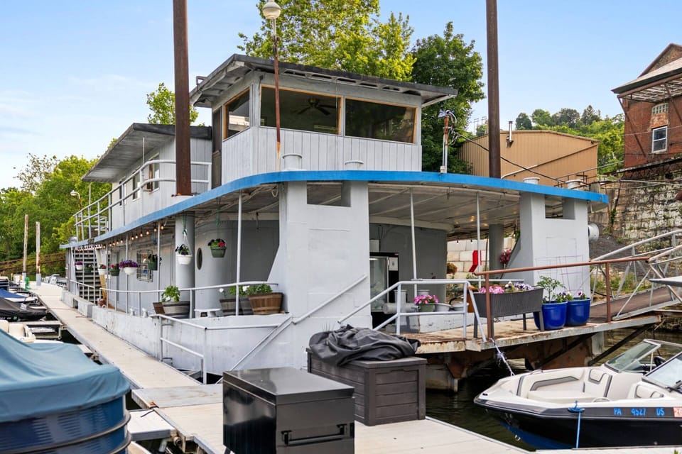 Houseboat exterior from the dock with outdoor seating area, potted plants, and two-story structure.