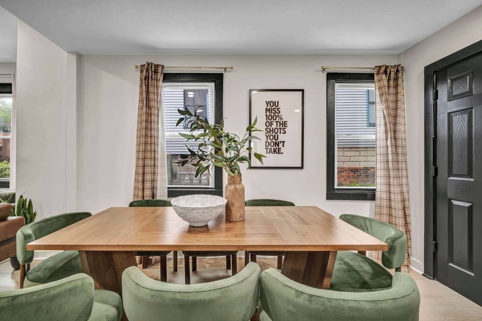 Dining room w/ a wood table & green upholstered chairs, framed art lining the walls.