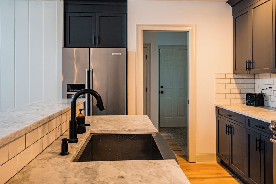 Full bath with a glass shower-tub, wood vanity, and patterned floor tile