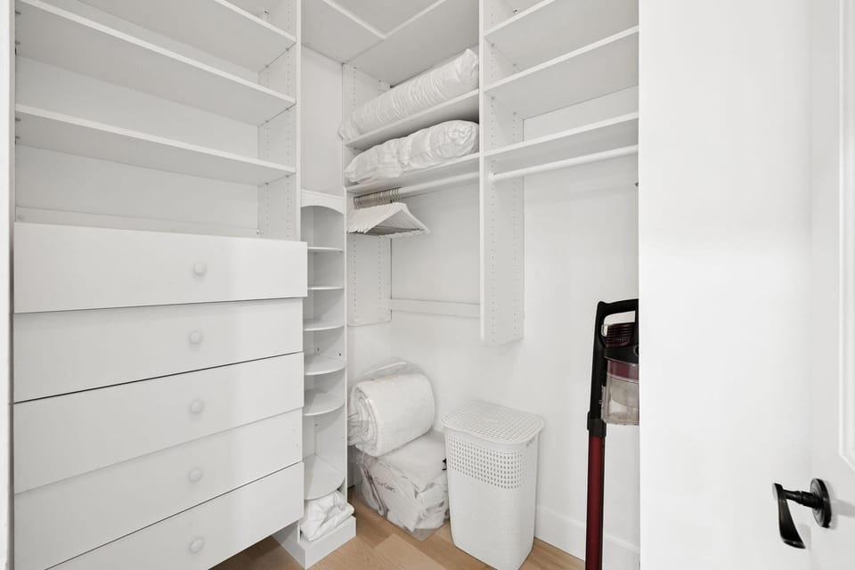 Walk-in closet with built-in white shelving, drawers, hanging rods, and a laundry hamper