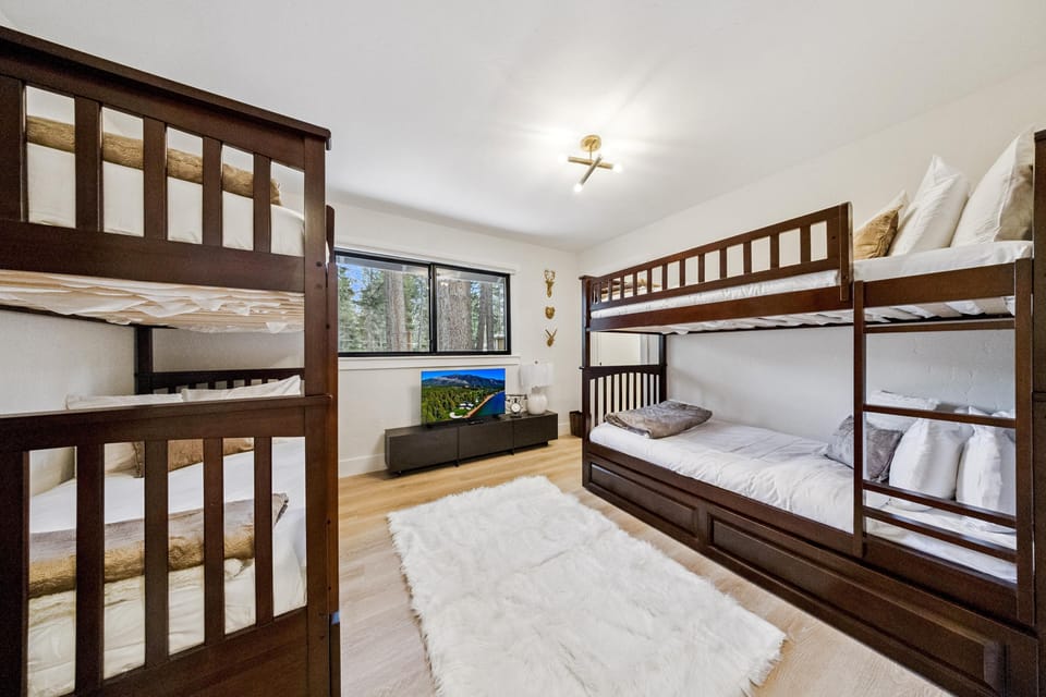 Bunk bedroom with two dark wood twin-over-full beds, a white shag rug, and TV on a low black console.