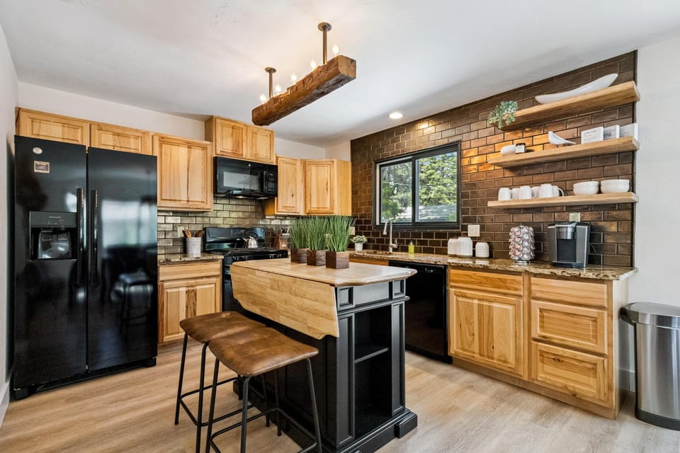 Kitchen with natural wood cabinets, black appliances, granite counters, and a black island topped with potted greenery.