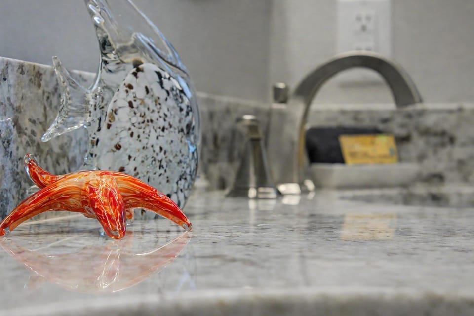 Close-up of decorative glass fish, starfish, and bathroom fixtures on granite countertop