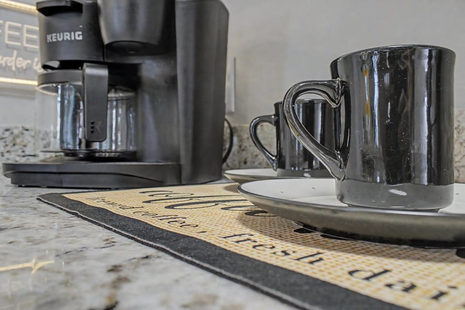 Keurig coffee maker beside black mugs on granite countertop