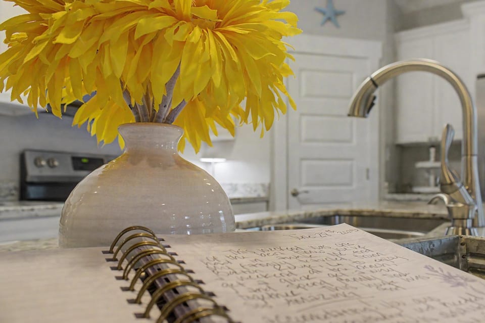 White vase with yellow flowers and open notebook on kitchen counter