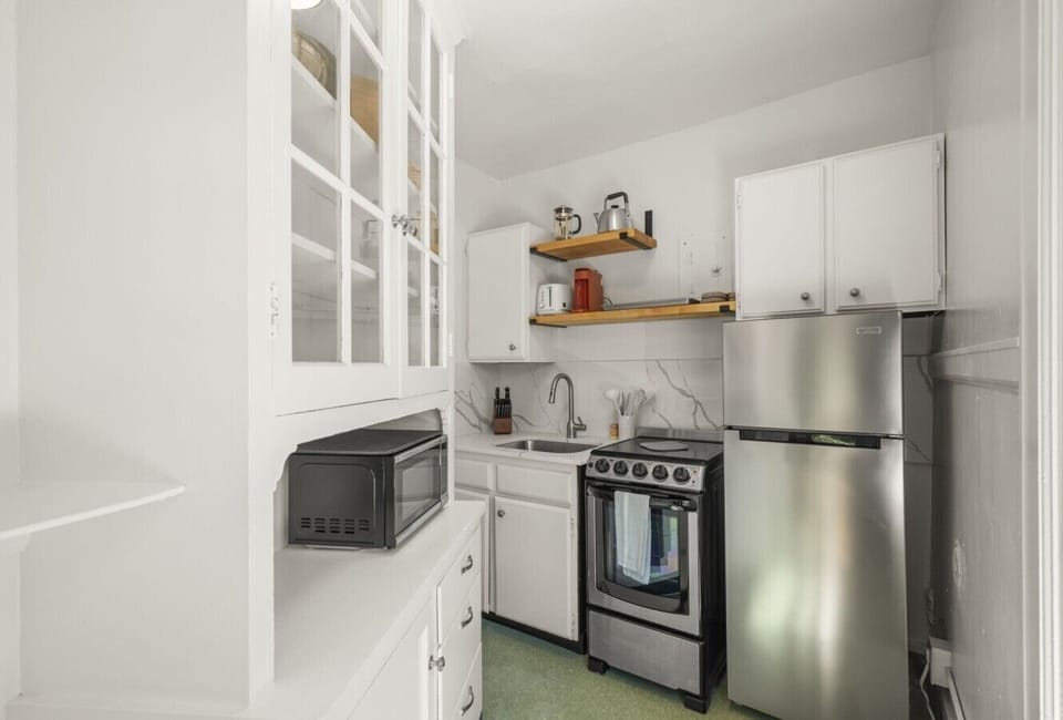 Bright and fully equipped kitchen featuring a gas stove, full-size refrigerator, microwave, French press coffee maker, cookware, dishes, and essentials for preparing meals at home