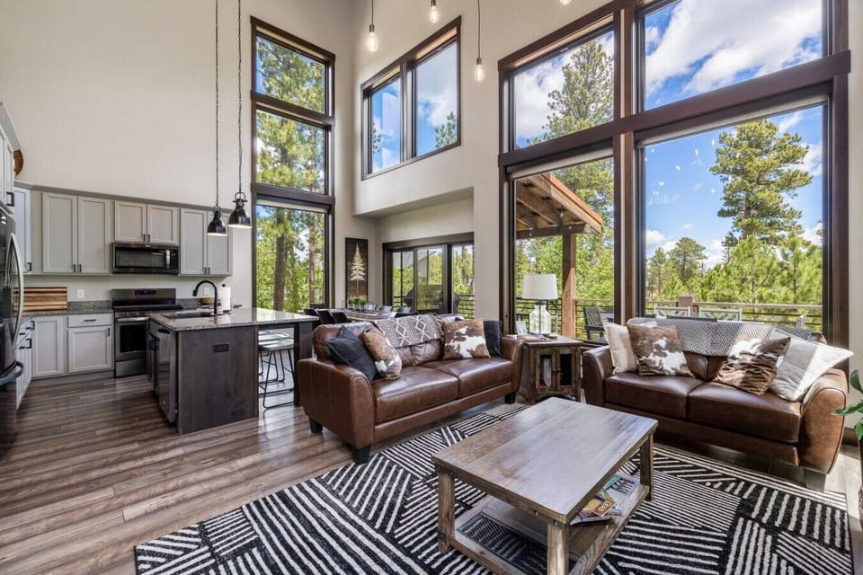 With pine views pouring through the oversized windows, leather seating, rich wood accents, and a dramatic lodge-style centerpiece, this space feels equal parts luxury retreat and mountain cabin comfort.