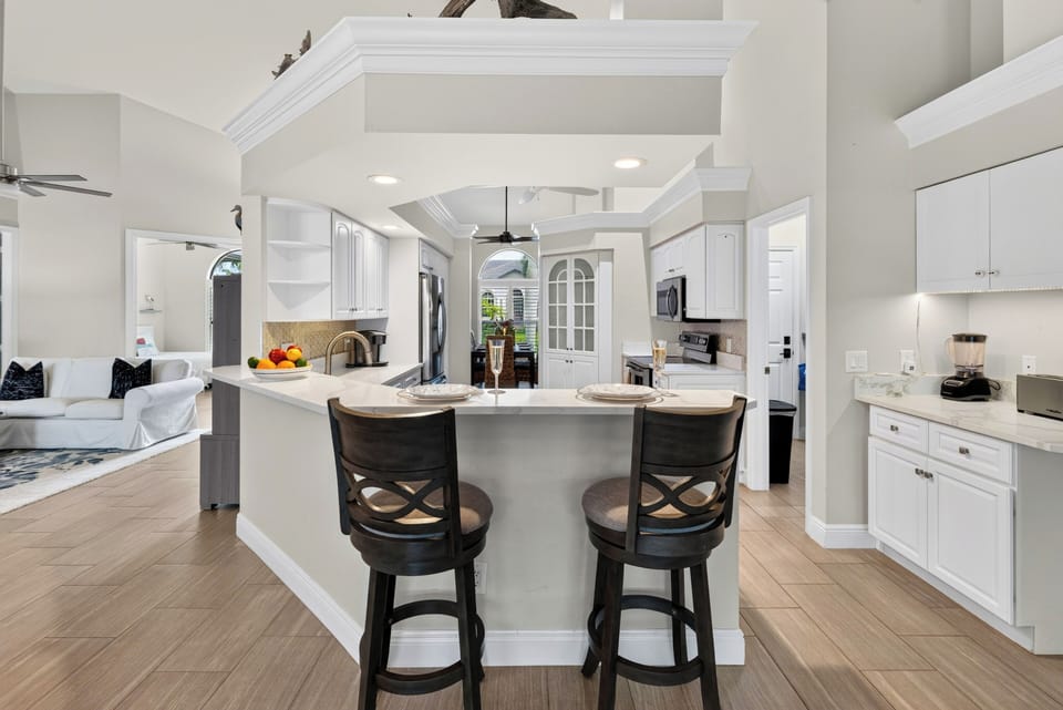 Modern chef's kitchen featuring a raised breakfast bar with seating, bright overhead recessed lighting, and crisp white cabinetry.