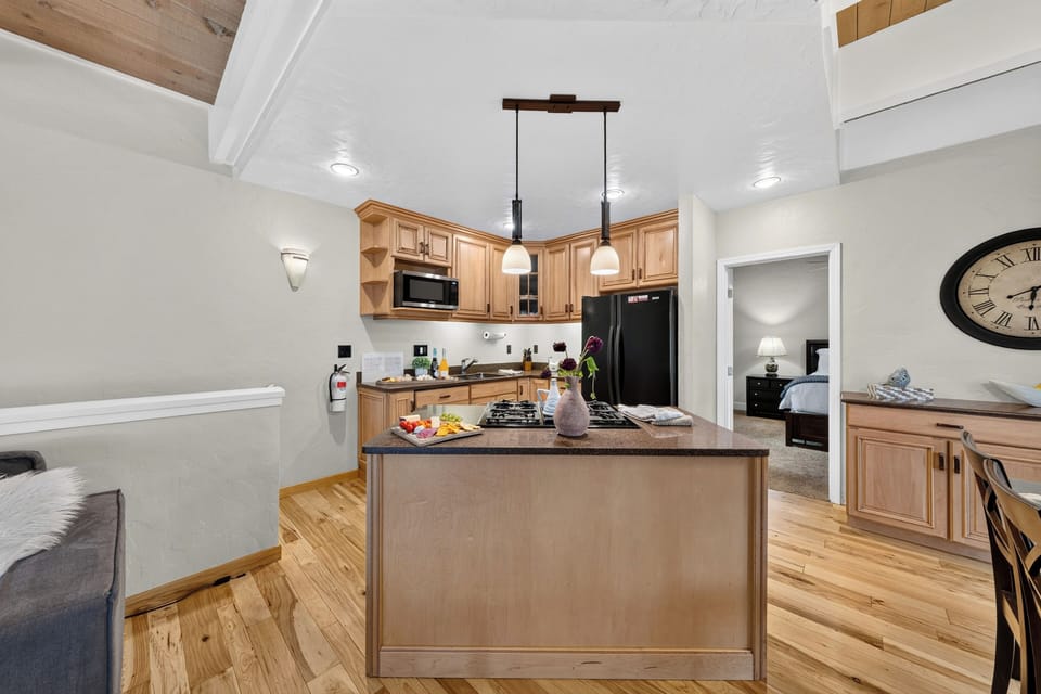 The modern kitchen includes a central island with overhead pendant lighting and light wood cabinetry.