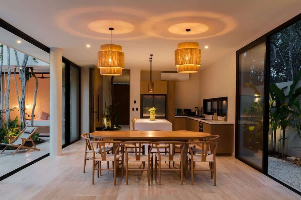 Open kitchen and dining area with rattan pendant lights, wooden table, and tropical garden views Tulum