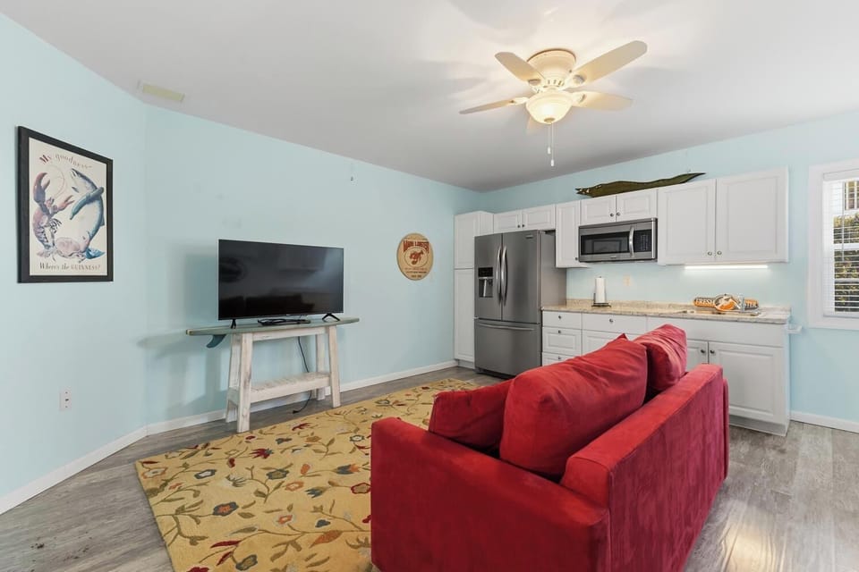 Unwind in your cozy living area with a plush red sofa, flatscreen TV, and fully equipped kitchen. The ceiling fan keeps you comfortable while you relax in this bright, beach-themed retreat.