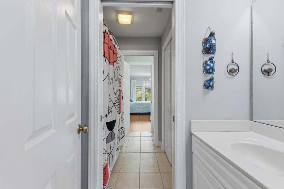 A hallway connects the private spaces of your rental, featuring charming coastal décor and tiled flooring leading to peaceful bedrooms ahead.