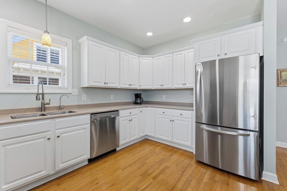A bright, modern kitchen awaits with stainless steel appliances, white cabinetry, and warm wood floors—your perfect space for morning coffee or preparing vacation meals together.