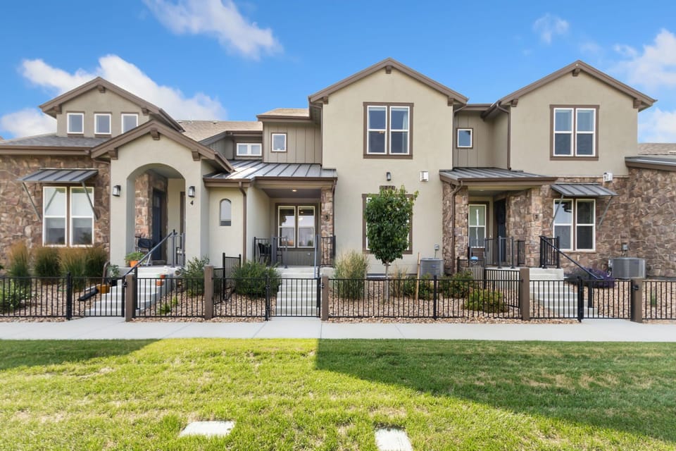 Modern multi-unit property with stone and stucco facades, featuring private patios and grassy lawn areas under clear blue skies.