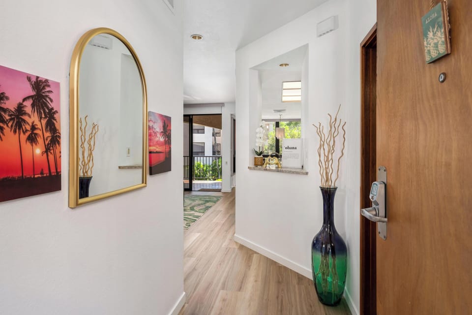 Step through your private entrance into a bright, welcoming space adorned with tropical artwork and warm wood floors that flow toward sunlit rooms beyond.