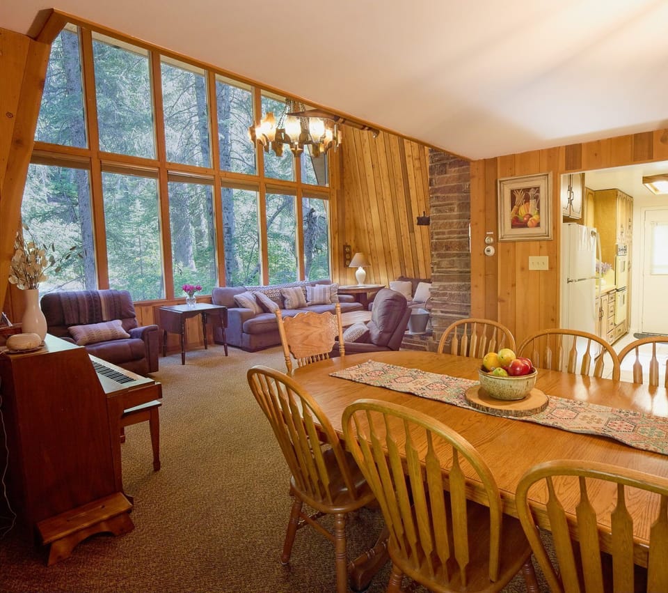 Dining area with wooden chairs and decorative table runner, forest views through the window