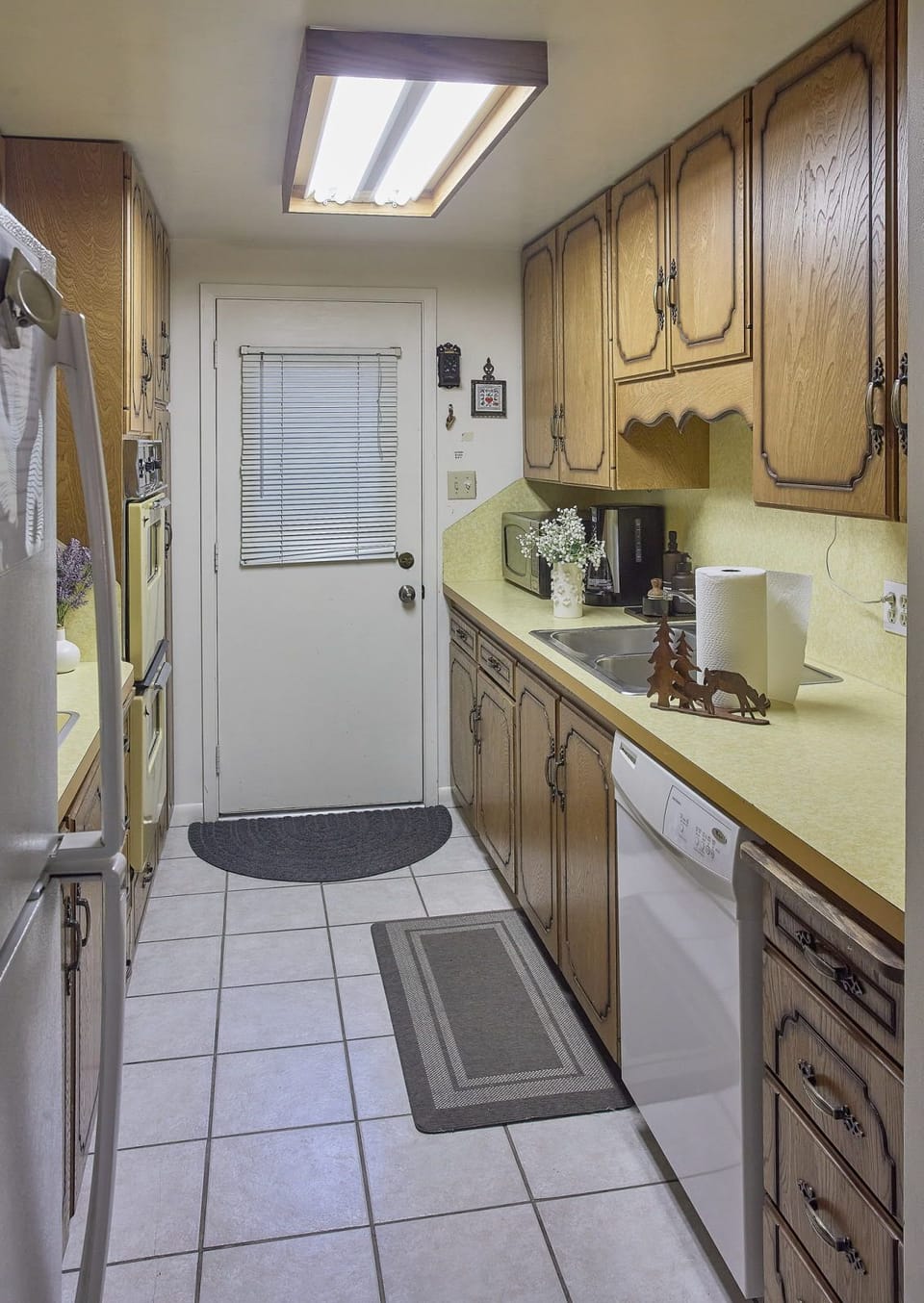 Narrow kitchen with vintage wood cabinets, exterior door, and a floral arrangement on the counter