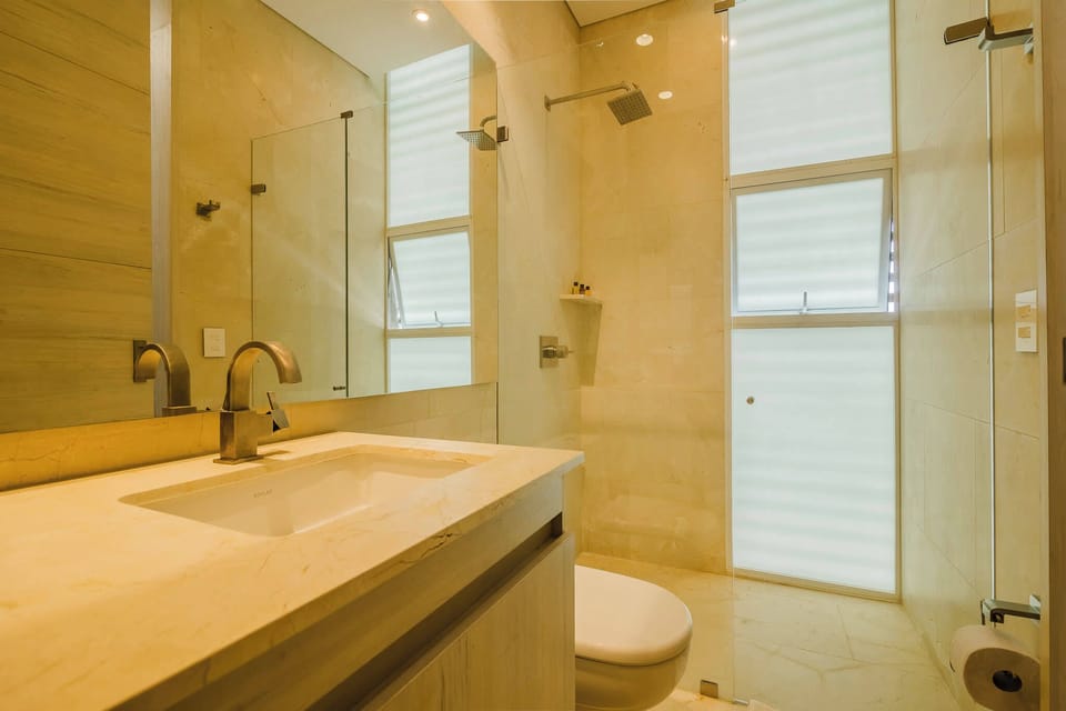 Sunlit bathroom w/ sink & glass-enclosed shower.
