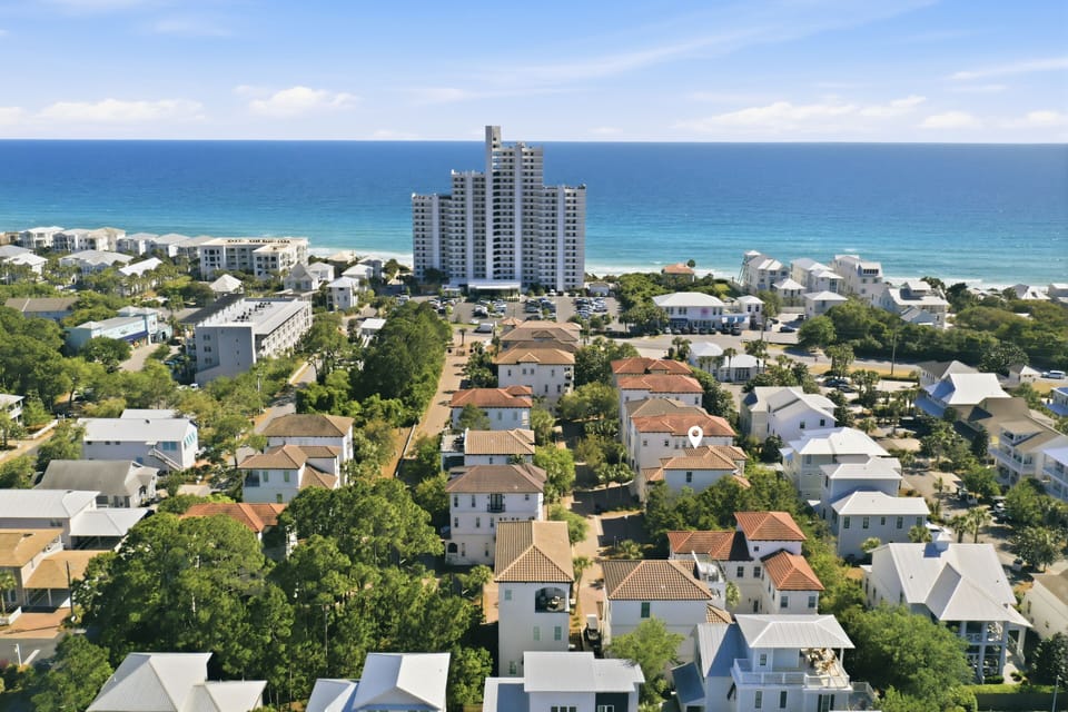 Aerial view of a coastal neighborhood with residential properties, high-rise buildings, and pristine beachfront along the turquoise Gulf waters.