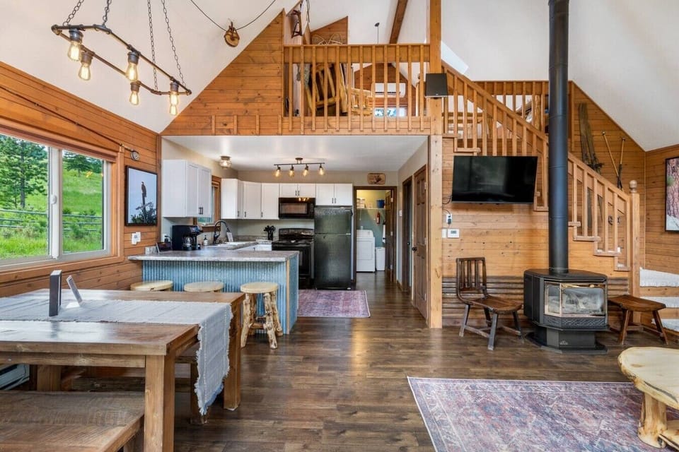 This open-concept view showcases the dining area, fully equipped kitchen, cozy living space, and charming loft above, creating a warm and inviting gathering place for everyone.