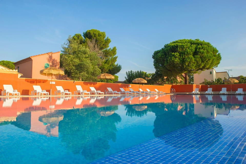 Clear blue water reflects the terracotta rooflines — the pool is the social heart of the 10-hectare domain.