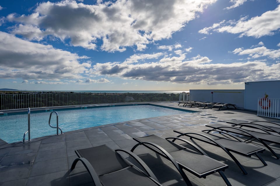 Sun loungers rim the rooftop pool deck, with open sky and coastal air stretching out beyond the railing.