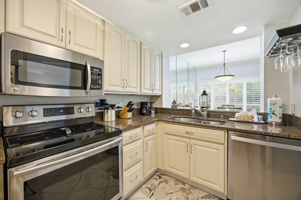 Granite countertops catch the overhead glow in this fully equipped kitchen, where stainless steel appliances meet bright cabinetry. A breakfast bar opens the view toward a sunlit dining area for easy mornings and effortless hosting.