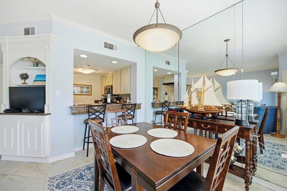 Polished wood and nautical accents define this airy dining space, where mirrored walls reflect the bright afternoon glow and open floor plan. A model ship adds a coastal touch to the warm, inviting atmosphere perfect for shared meals.