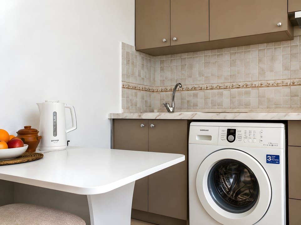 Sink, cabinetry. Samsung washing machine, Bosch kettle, and table are in view.