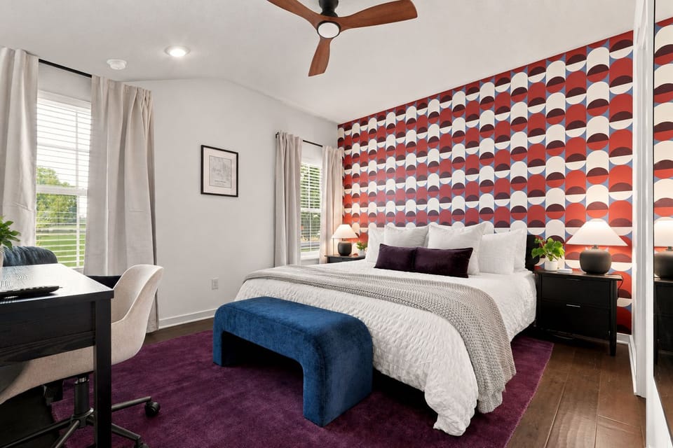 Stylish king bedroom with bold accent wall, desk, and natural light