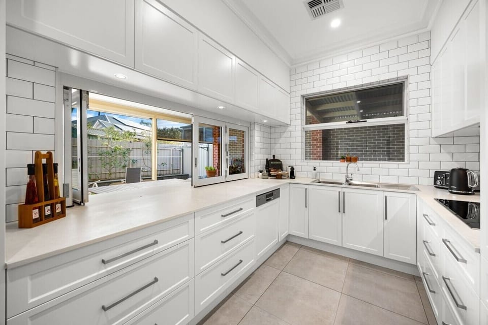 The bright galley-style kitchen is fully equipped for home cooking, with quality appliances, generous bench space, and bifold windows opening directly to the outdoor bar for seamless entertaining.