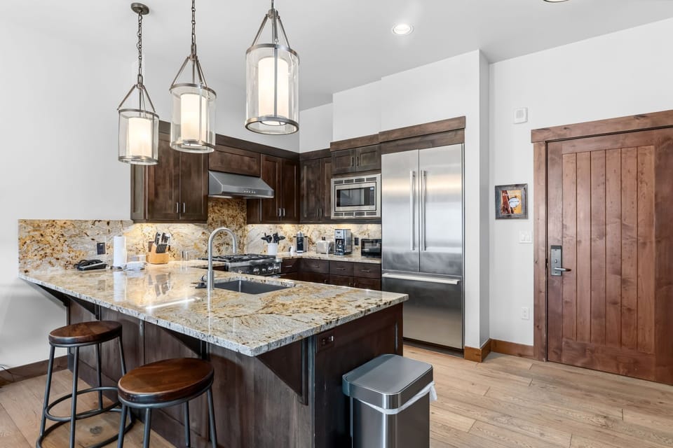 Step into your gourmet kitchen where granite countertops gleam under elegant pendant lights. Stainless-steel appliances and rich wood cabinetry create the perfect space for cooking memorable vacation meals together.
